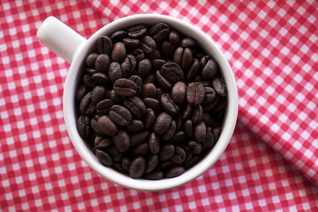 Flat lay of coffee beans in white ceramic cup on tablecloth