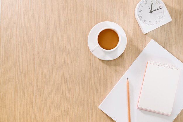 Flat lay of coffee cup, clock, pencil and a notebook.