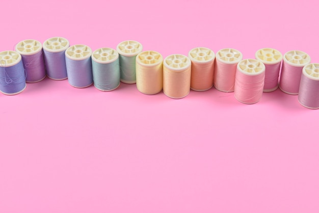 Flat lay of colored thread rolls for sewing on pink background.