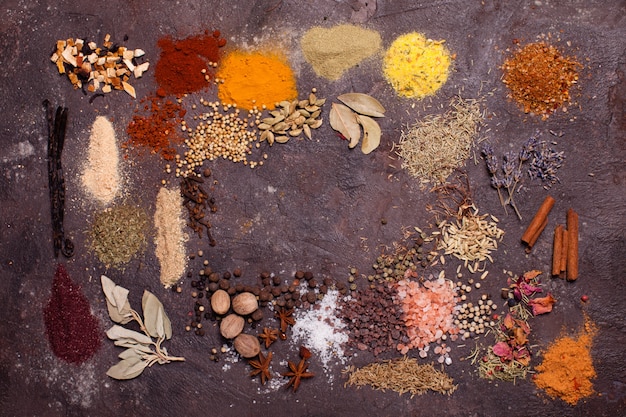 Flat lay composition frame of various spices over brown slate background, top view