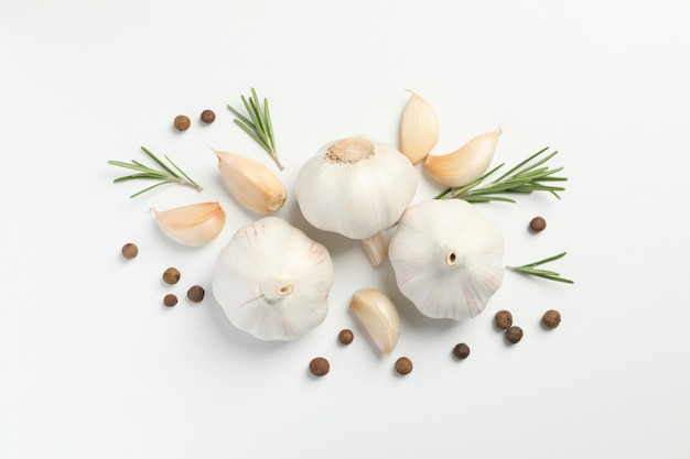 Flat lay of composition, garlic bulbs, slices, spice, parsley, rosemary on white