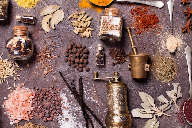 Flat lay composition of various spices and mortars over brown slate background, top view