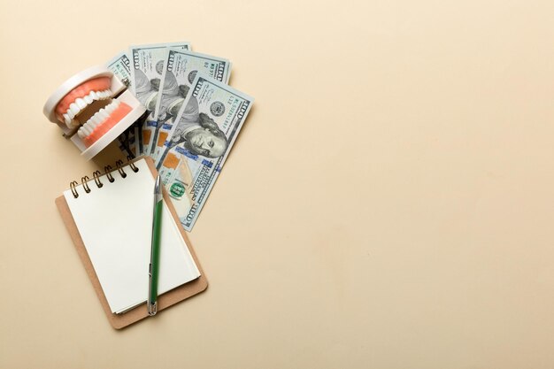 Flat lay composition with educational dental typodont model and money with notebook on colored table top view Expensive treatment