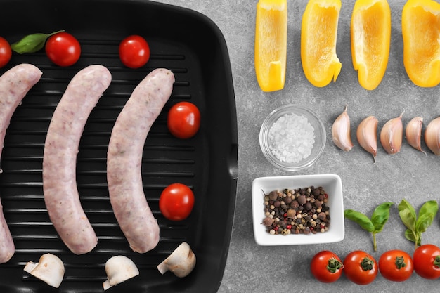 Flat lay composition with grill pan sausages and vegetables on grey background