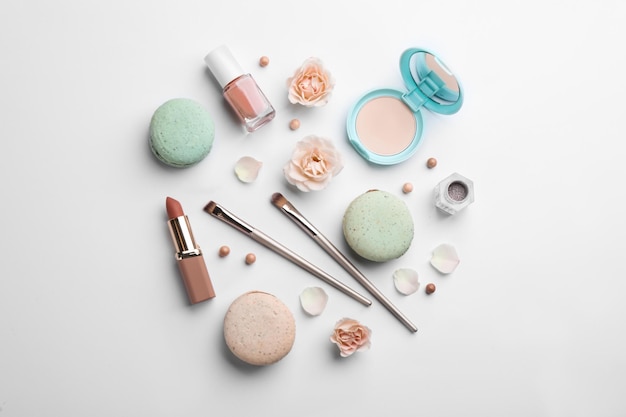 Flat lay composition with makeup products roses and macarons on white background