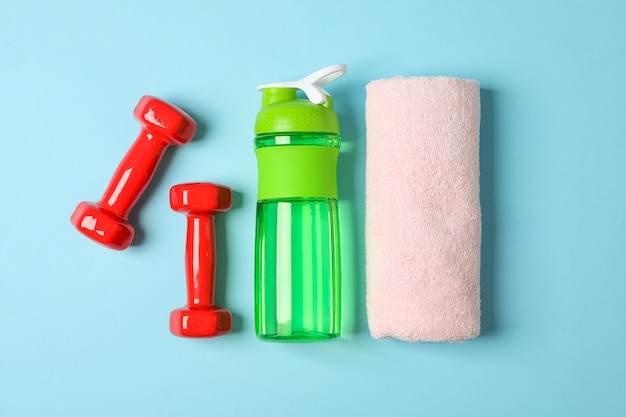 Flat lay composition with towel, dumbbells and fitness bottle on blue background