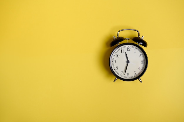 Flat lay composition with a Vintage black alarm clock on yellow background with copy space to add text. Back to School and Teachers Day Concepts, Business, Organization, Time Management