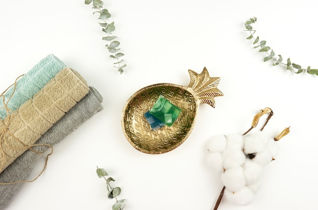 A flat lay of cotton towels, hand made soap, a pot with eucalyptus and a branch of cotton on a white table in a modern bathroom