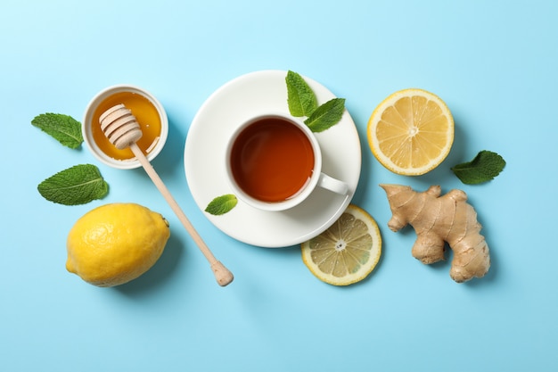 Flat lay. Cup of tea, lemon, ginger, mint, honey and dipper on blue, copy space