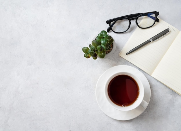 Flat lay cup of tea notepad pen eyeglass and succulent plant on a light background Work women's concept Top view and copy space