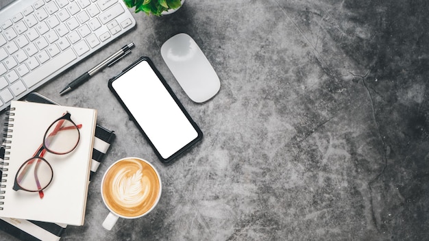 Flat lay Dark office desk with keyboard computer blank screen smart phone pen eyeglass mouse notebook and coffee Top view with copy space Mock up