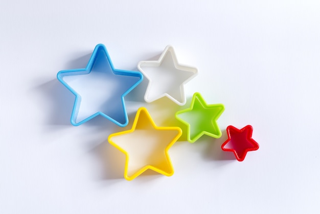 Flat lay of decorative colorful plastic cookie cutters in the shape of stars for cooking homemade Christmas pastry on white