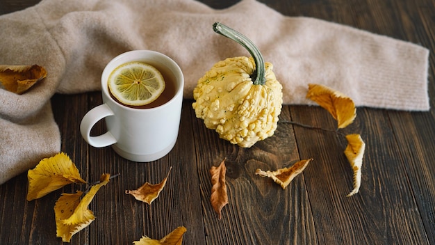 Flat lay of decorative pumpkins dried leaves accessories and tea with lemon in cup on wooden background Top view copy space Autumn concept