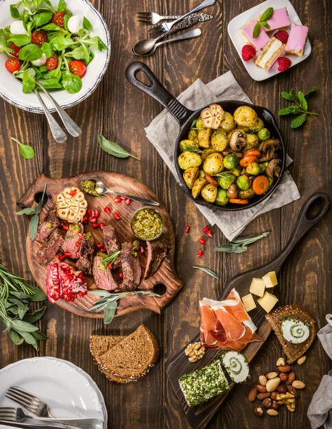 Flat lay of delicious dinner table with roasted meat steak, appetizers and desserts. 