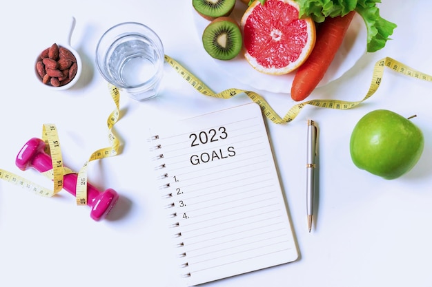 Flat lay of fruits vegetables dumbbell tape measure and a glass of water on white table background Clean eating and exercise for good health concept Organic food diet concept Top view copy space