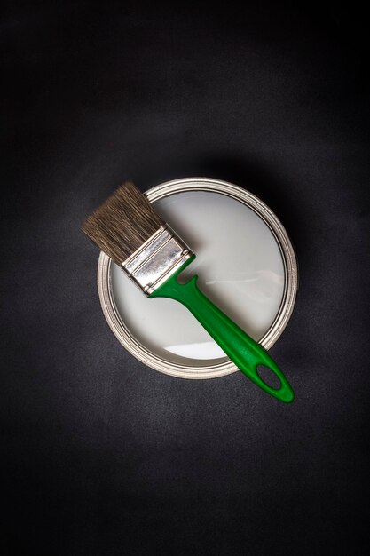 Flat lay , green brush on iron can, with paint on black textured background.