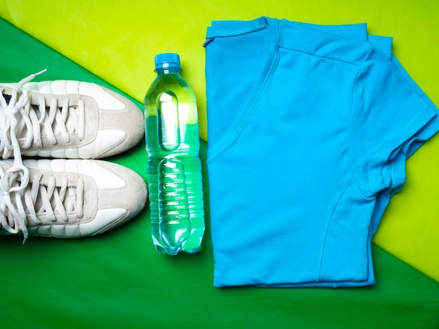 Flat lay on green sport mat background of sport tshirt pants sneaker fitness items top view