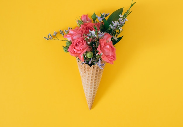 Flat lay Ice Cream Cone with colorful bouquet on yellow, copy space