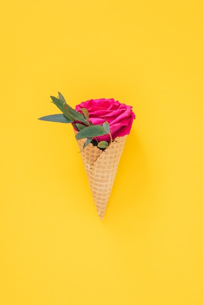 Flat lay Ice Cream Cone with pink rose on yellow, copy space