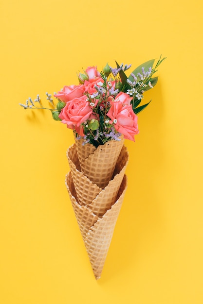 Flat lay Ice Cream Cones with colorful bouquet on yellow, copy space