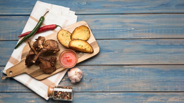 Flat lay lamb chops on wooden board with potatoes and sauce with copy-space