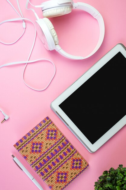 Flat lay of laptop, earphones, digital gadget, soft pink background with copy space