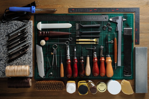 Flat lay of leather working tools on wooden desk