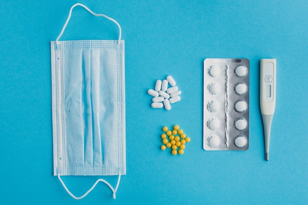 Flat lay of medical accessories pills washing mask and thermometer on blue background