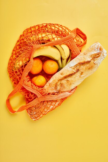 Flat lay Mesh grocery shopping eco friendly bag fruits baguette on yellow canvas background Zero waste cconcept Local farmers market shopping mall top view copy space Plastic free items