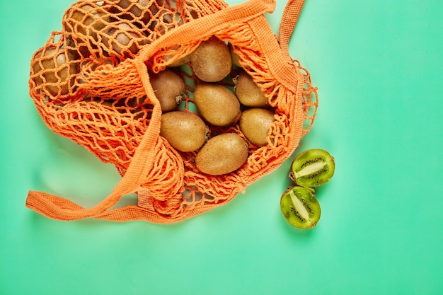 Flat lay Mesh grocery shopping eco friendly bag with kiwi on green canvas background Zero waste cconcept Local farmers market shopping mall top view copy space Plastic free items