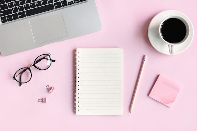 Flat lay of mobile phone, a cup of coffee, glasses and office stationary of businesswoman on pink