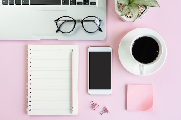 Flat lay of mobile phone, a cup of coffee, laptop and stationary of student on pink table. Business and technology, distance education concept top view and copy space.