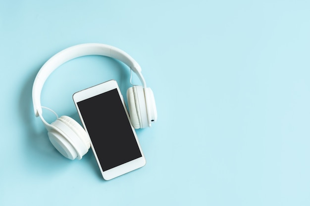 Photo flat lay of mobile phone and wireless headphones on blue color background. top view and copy space