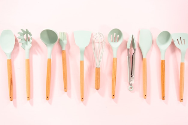 Flat lay. New blue silicone kitchen utensils with wooden handles on a pink background.