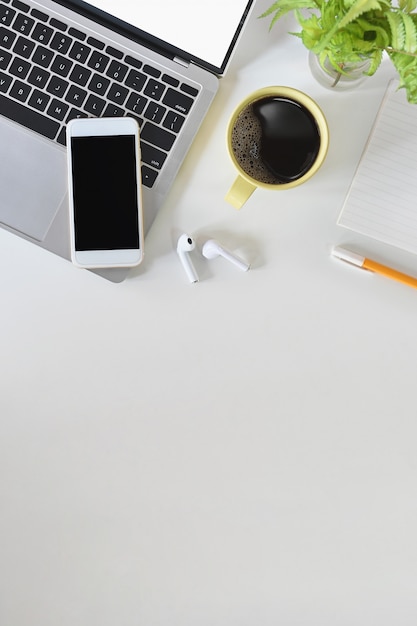 Flat lay office desk laptop, mobile phone, earphones, notebook, pen and coffee cup with space.