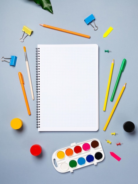 Flat lay office desk with a blank page of a notebook with a pen pencils watercolor and other stationery Top view flat lay