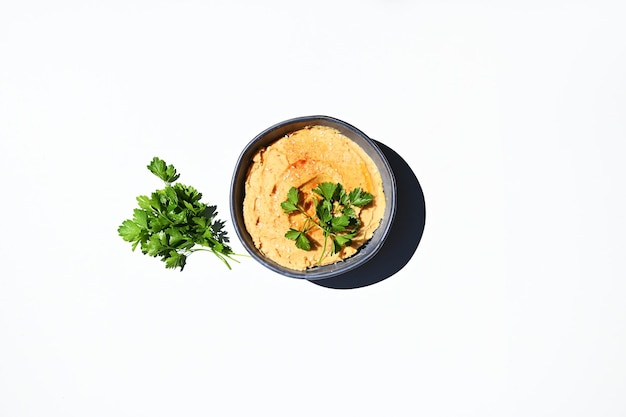 Flat lay Parsley and bowl with topped chickpea hummus sprinkled with paprika isolated on white background Copy space