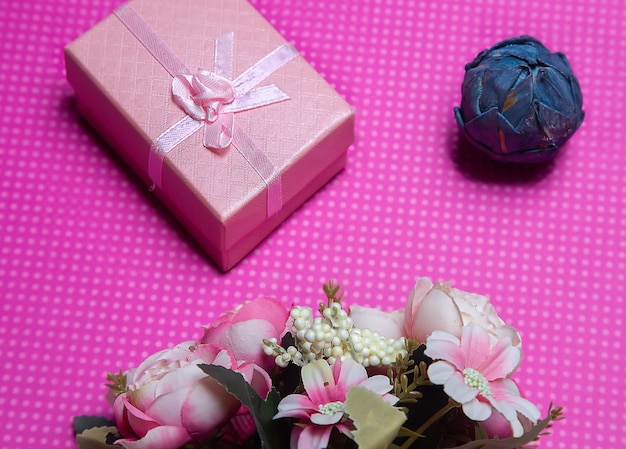 A flat lay photo of a bouquet of flowers a gift in the form of a box and accessories on a pink