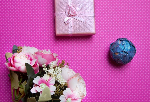 A flat lay photo of a bouquet of flowers a gift in the form of a box and accessories on a pink