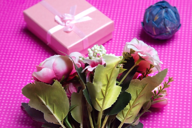 A flat lay photo of a bouquet of flowers a gift in the form of a box and accessories on a pink