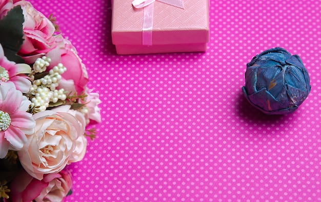 A flat lay photo of a bouquet of flowers a gift in the form of a box and accessories on a pink