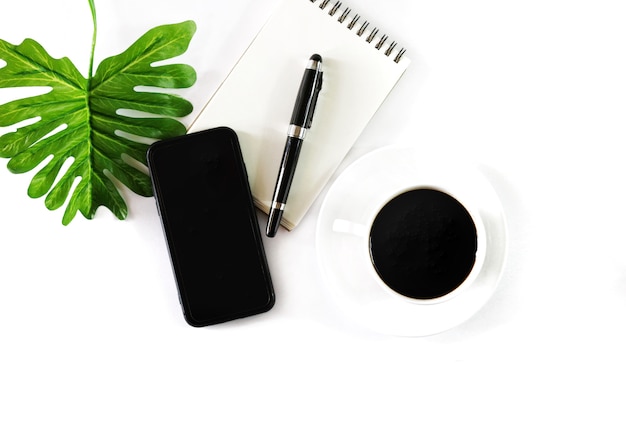 Flat lay photo with notebook, coffee cup, pen, smartphone and tropical leave