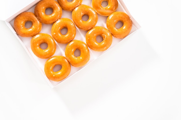 Flat lay. Plain glazed store-bought doughnuts in a white paper box.