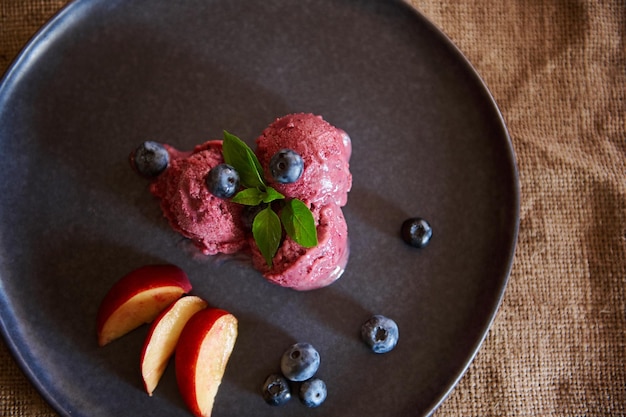 Flat lay Raw vegan dessert Refreshing blueberry sorbet ice cream with slices of ripe juicy peach and mint leaves