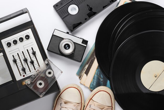 Flat lay retro media composition. Equalizer tape recorder, vinyl records, oldfashioned sneakers, camera, video cassette on a white