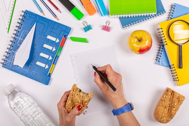 flat lay of school supplies on a minimalist blue space. Woman eats sandwich. Healthy snack at office workplace. Eating organic vegan meals