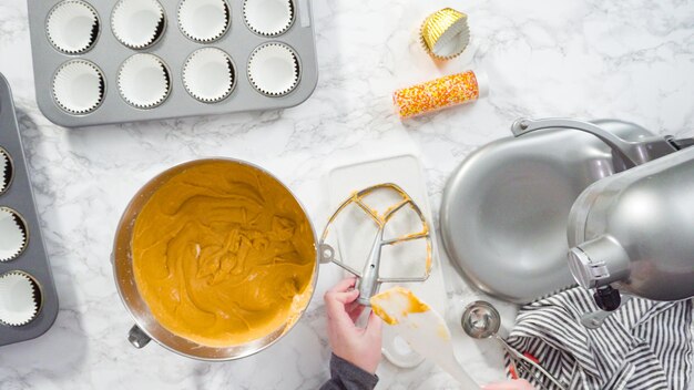 Flat lay. Scooping pumpkin spice cupcake batter with batter scoop into a cupcake pan with liners.