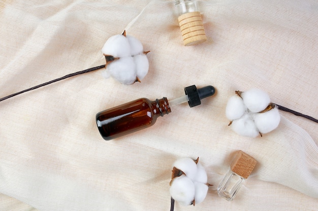 Flat lay of Serum glass bottle with pipette and beautiful cotton flower on cloth texture background, Concept of natural cosmetic, skinimalism, copy space.