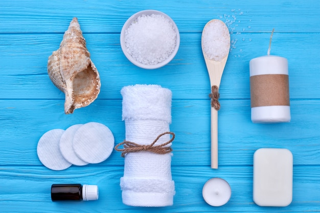 Flat lay set of bathroom accessories onn blue wooden desk. Towel with seashell candle and salt.