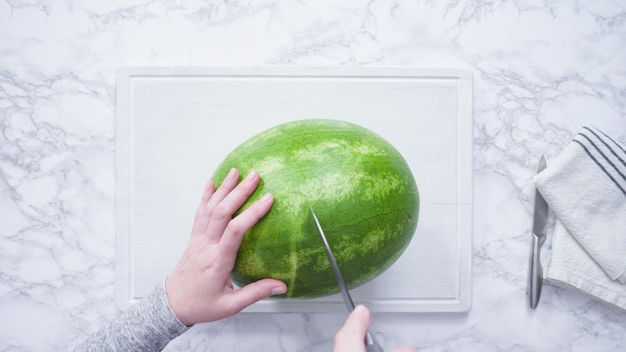 Flat lay. Slicing red watermelon into small pieces on a white cutting board.